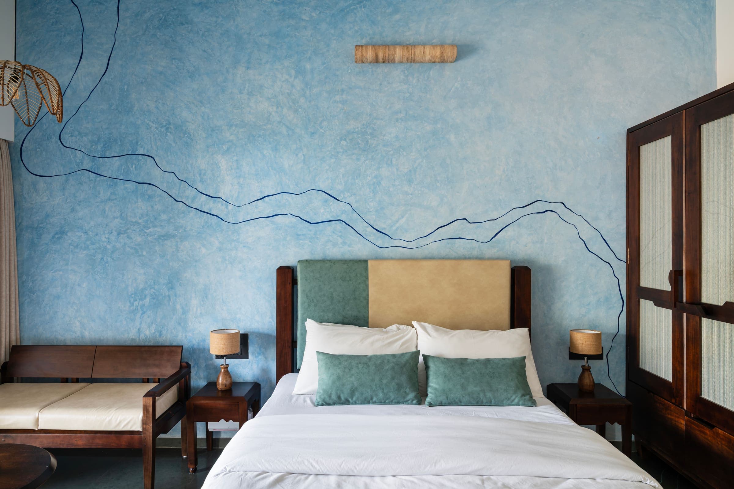 Swarna's queen bed against the river-blue wall, with its hand-drawn river contours